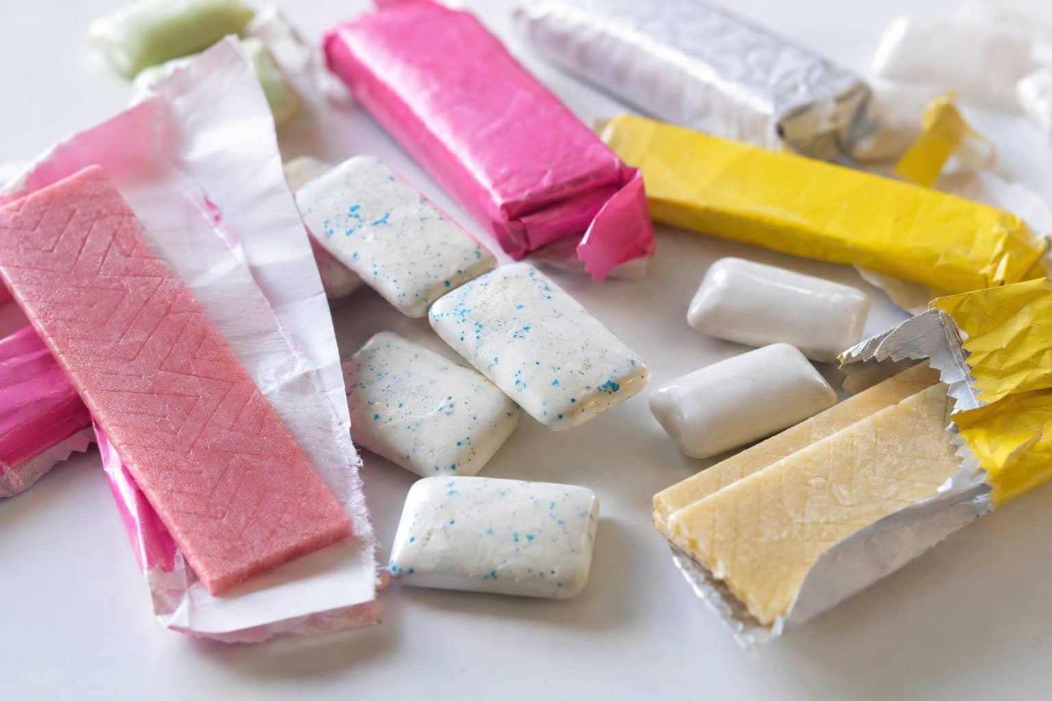 Chewing-gums de marque variée éparpillés sur une surface, gros plan montrant la texture et les couleurs